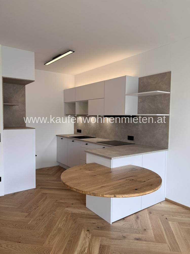 Moderne Küche mit weißen Schränken, Holztisch und Fischgrätparkettboden.