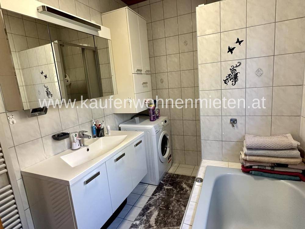 Badezimmer mit Waschbecken, Spiegelschrank und Badewanne, inklusive Waschmaschine.