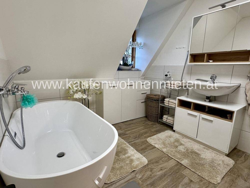 Modernes Badezimmer mit freistehender Badewanne, Waschtisch und Dachschräge.