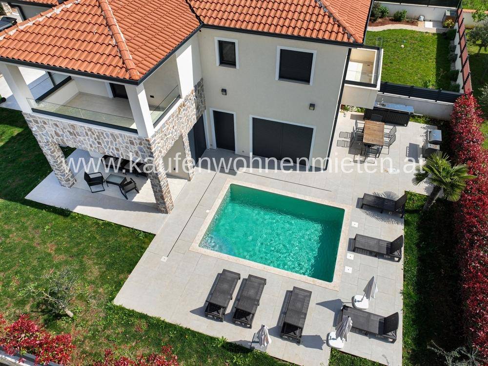 Luftaufnahme einer modernen Villa mit großem Pool, Sonnenterrasse und gepflegtem Garten.