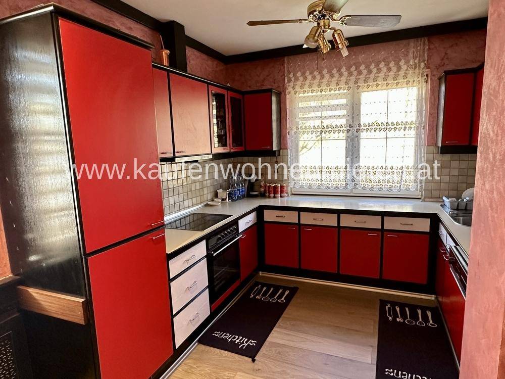 Küche mit roten und schwarzen Schränken, integrierten Geräten und Deckenventilator.