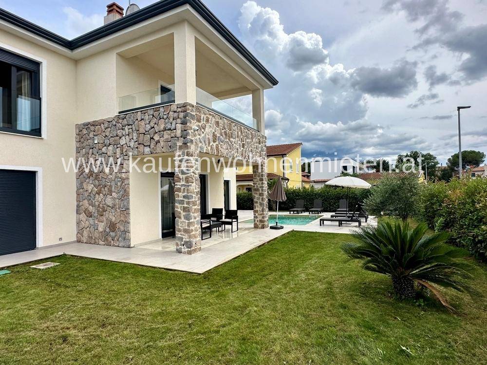Modernes Haus mit gepflegtem Garten, Poolbereich und Steinverkleidung unter bewölktem Himmel.