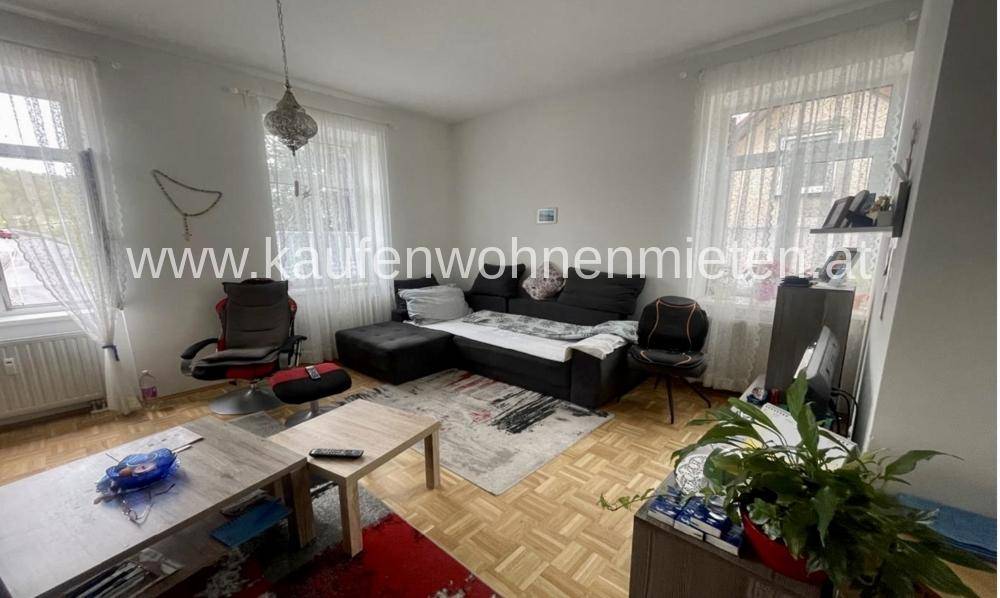 Gemütliches Wohnzimmer mit Sofa, Couchtisch und Parkettboden, gut beleuchtet durch zwei Fenster.