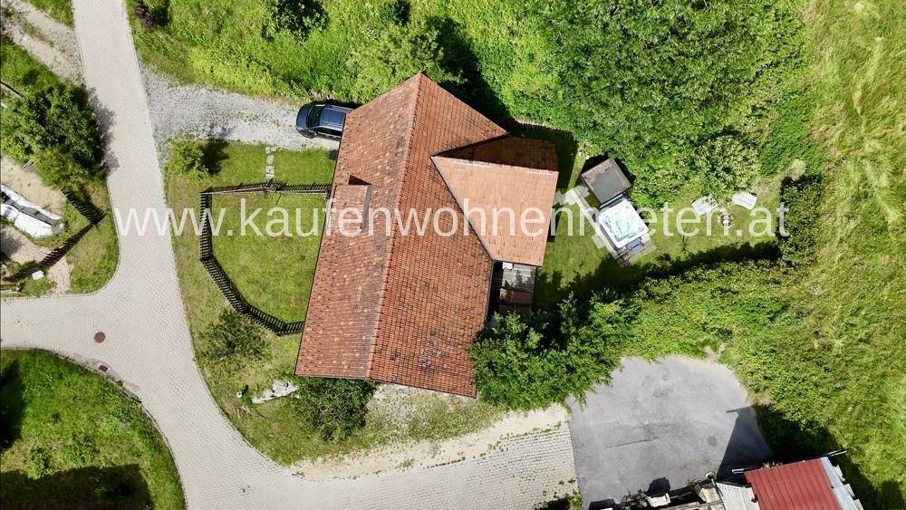 Luftaufnahme eines Hauses mit rotem Ziegeldach, umgeben von viel Grün und Bäumen.