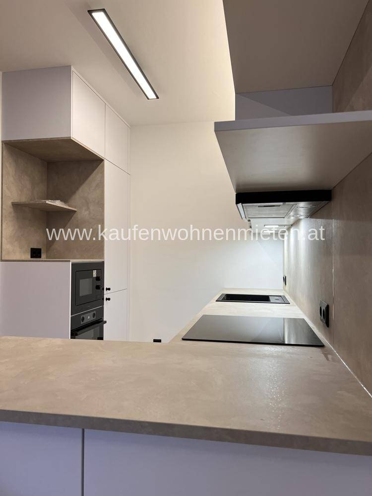 Moderne Einbauküche mit Induktionskochfeld, Backofen und hellen Arbeitsplatten.