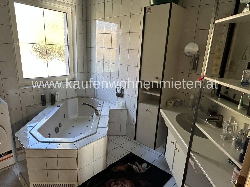 Badezimmer mit Eckbadewanne, Fliesen und Fenster für natürliches Licht.