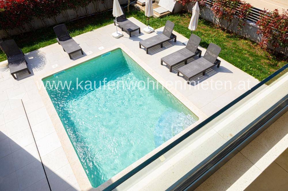Blick von oben auf den privaten Swimmingpool mit Liegestühlen und gepflegter Umgebung.