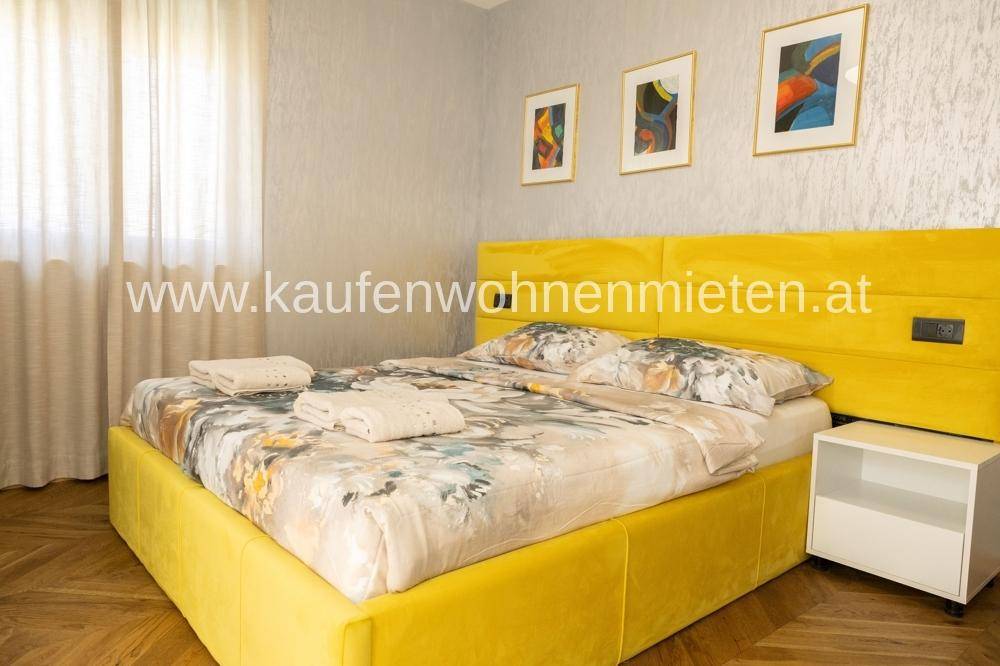 Helles Schlafzimmer mit auffälligem gelbem Bett und Nachttisch, dekoriert mit modernen Bildern.