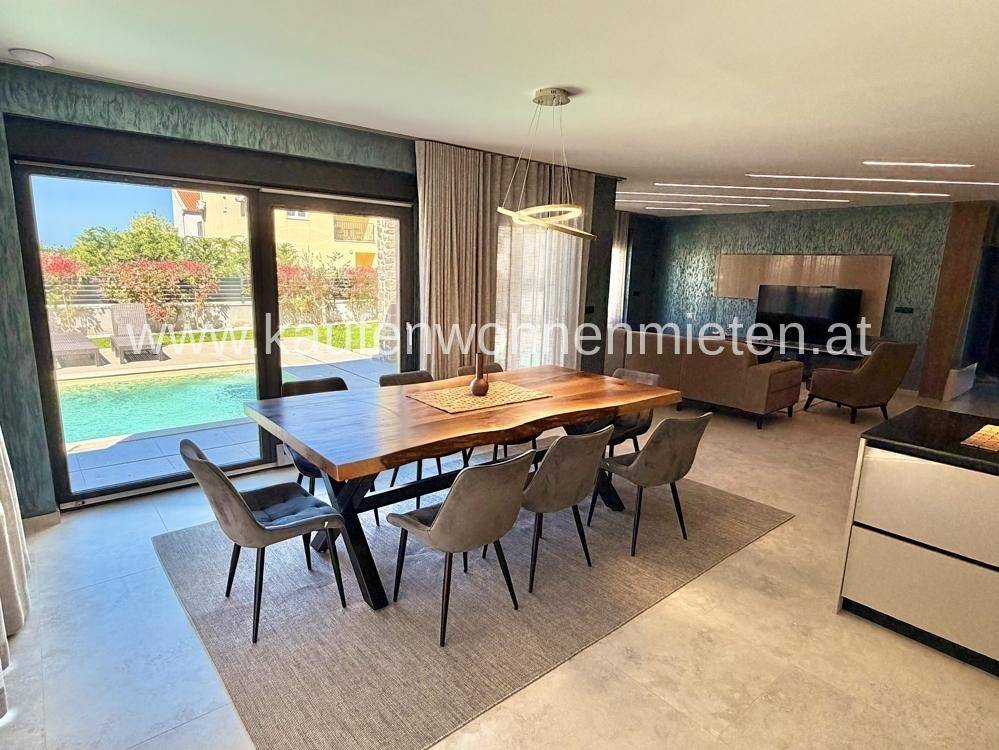 Heller Essbereich mit großem Holztisch und Zugang zur Terrasse mit Poolblick.
