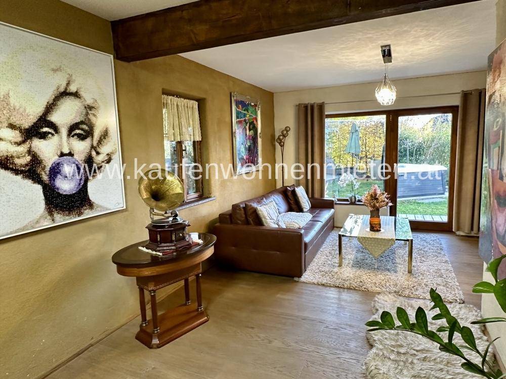 Gemütliches Wohnzimmer mit Ledersofa, Kunstwerken und Zugang zum Gartenbereich.