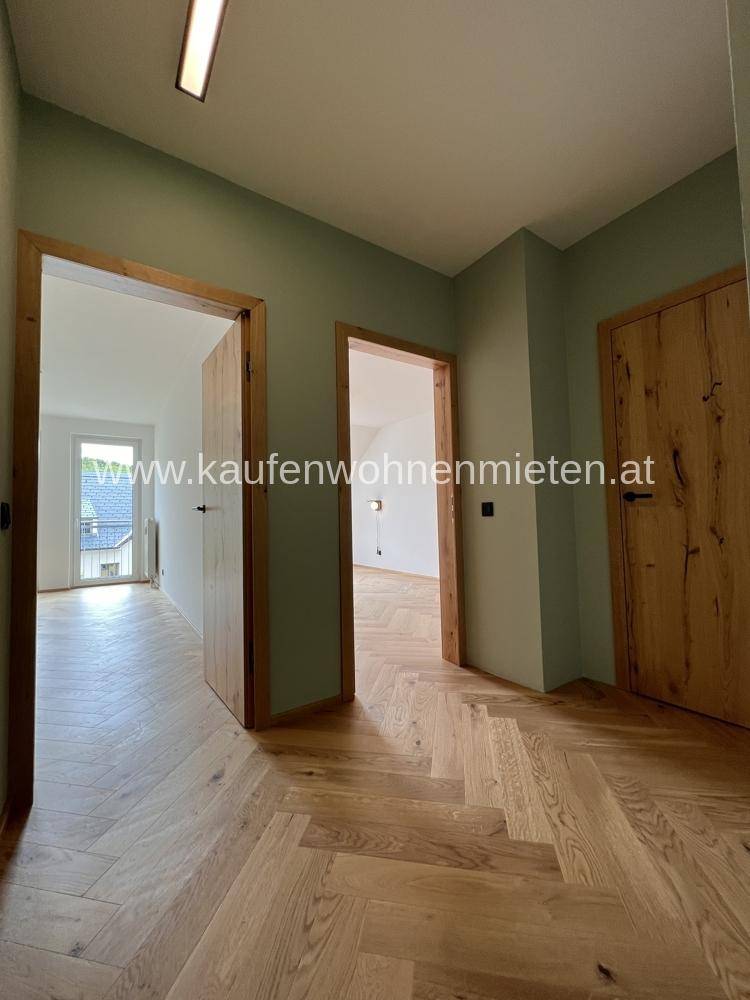 Flur mit hellem Fischgrätparkettboden, grünen Wänden und Holztüren zu den Zimmern.