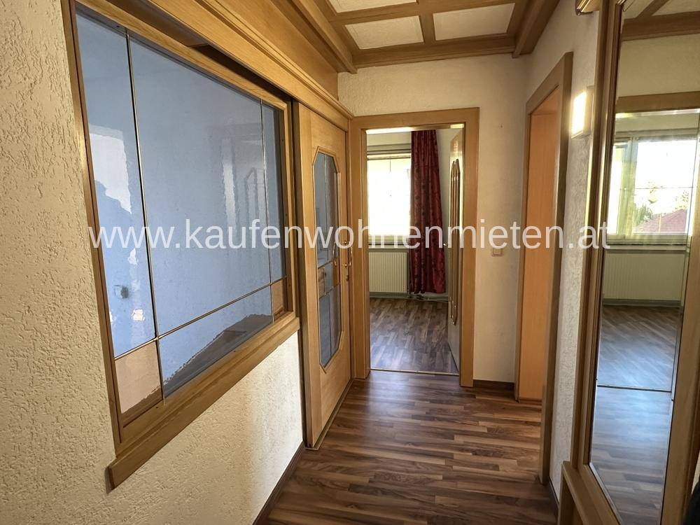 Heller Eingangsbereich mit Holzboden und Holzdecke, der zu weiteren Räumen führt.