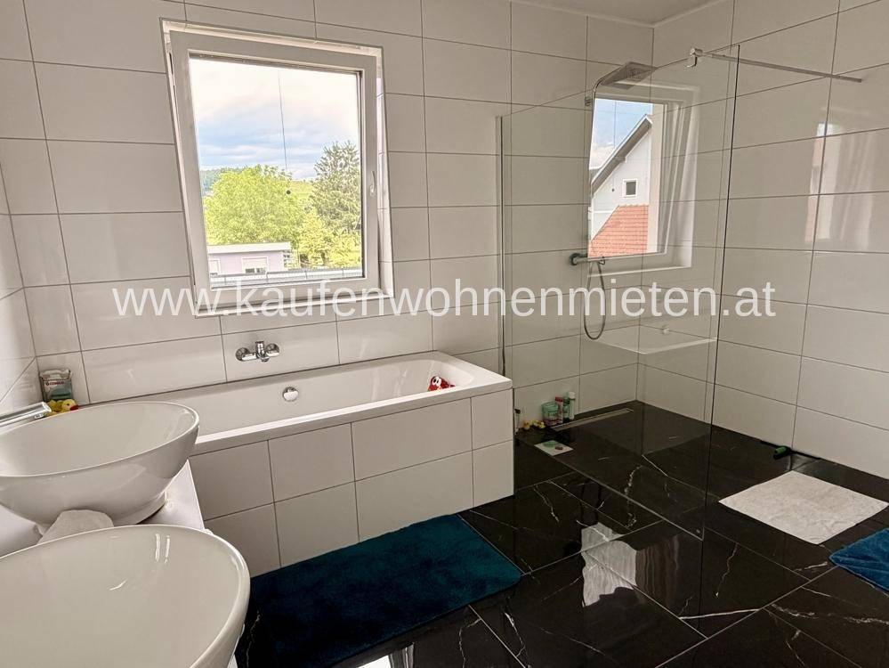 Modernes Badezimmer mit Badewanne, ebenerdiger Dusche, zwei Waschbecken und Fenster.