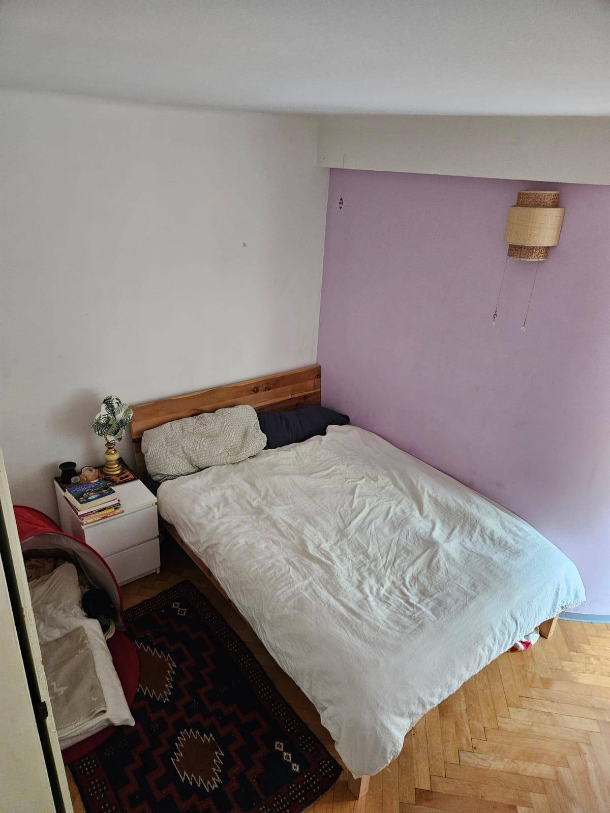 Schlafzimmer mit Holzbett, Fischgrätparkett und lila Akzentwand.