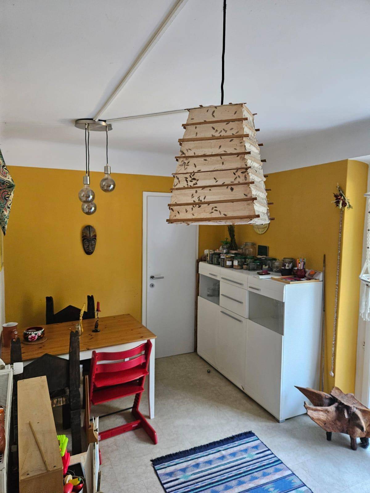 Essbereich mit gelber Wand, Holztisch und moderner Hängelampe.