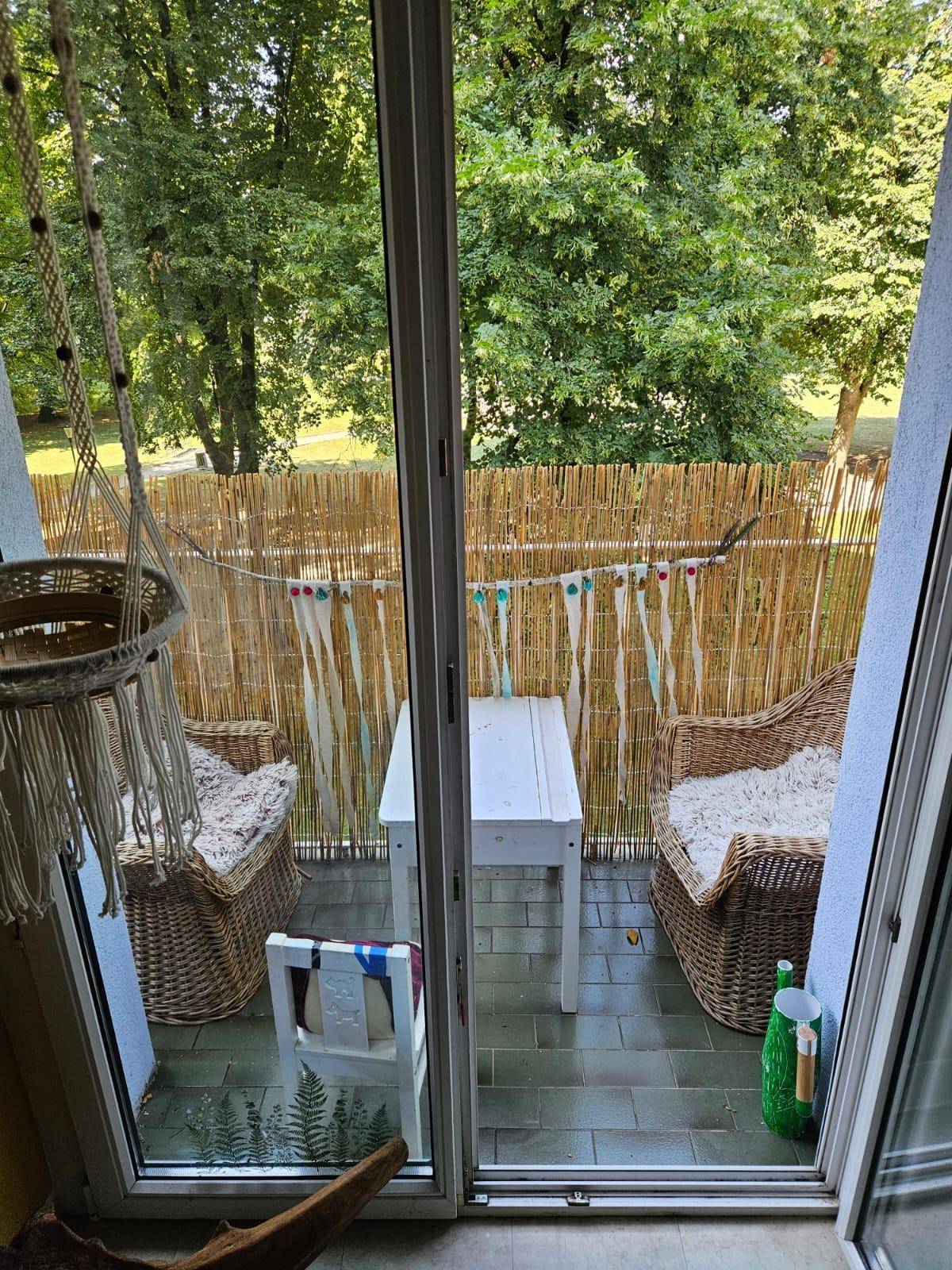 Gemütlicher Balkon mit Korbmöbeln und Sichtschutz, umgeben von viel Grün.