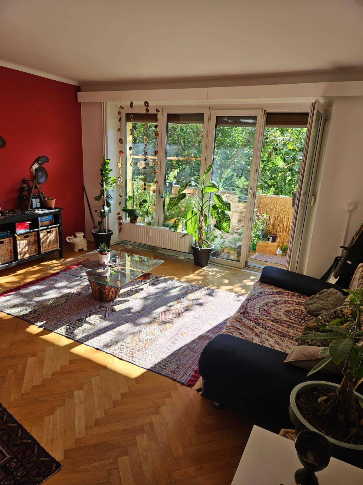 Sonniges Wohnzimmer mit Holzboden, gemütlichem Sofa und Blick ins Grüne.