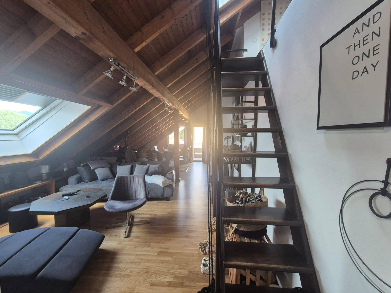 Geräumiges Wohnzimmer im Dachgeschoss mit Holzbalken, Dachfenster und gemütlicher Sitzecke.