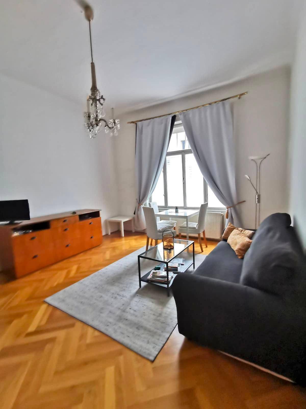 Geräumiger Wohnbereich mit Parkettboden, Sofa und Esstisch am Fenster.