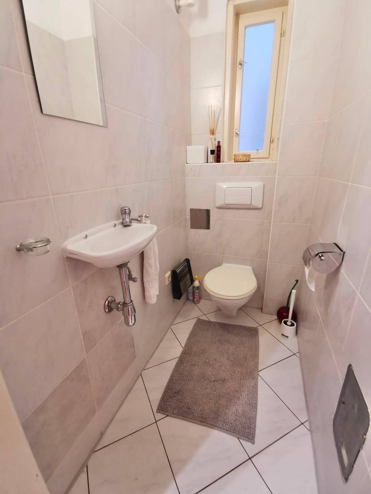 Kleines Gäste-WC mit Fenster, Wand-WC und Handwaschbecken.