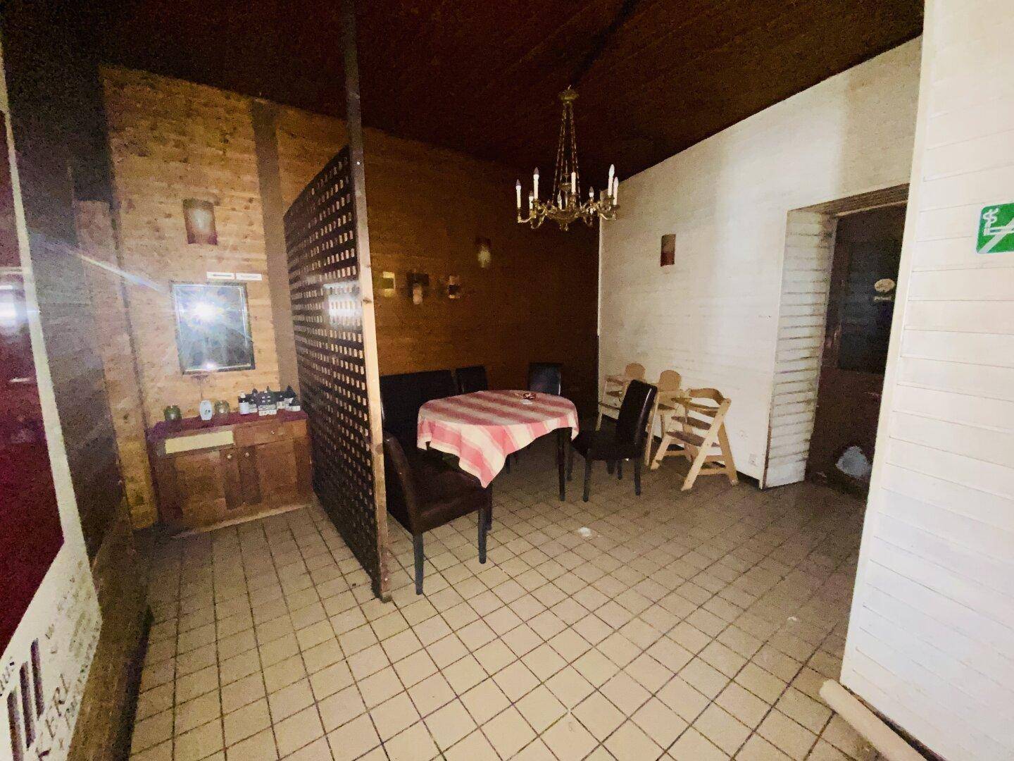 Rustikaler Restaurantbereich mit Holzwänden, gefliestem Boden und einem Kronleuchter über einem kleinen Esstisch.