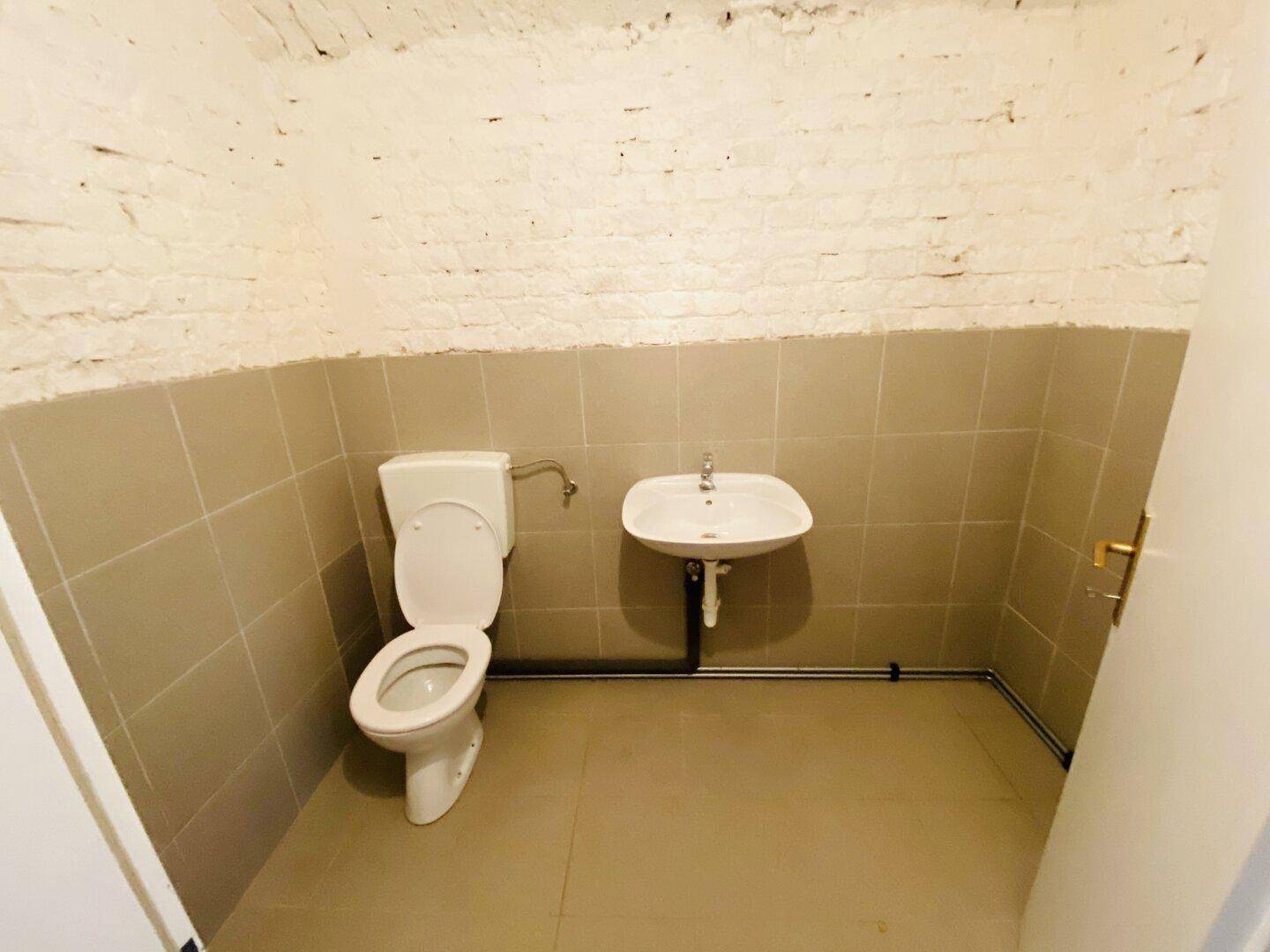 Kleines Gäste-WC mit beigefarbenen Fliesen, weißer Toilette und einem Waschbecken.