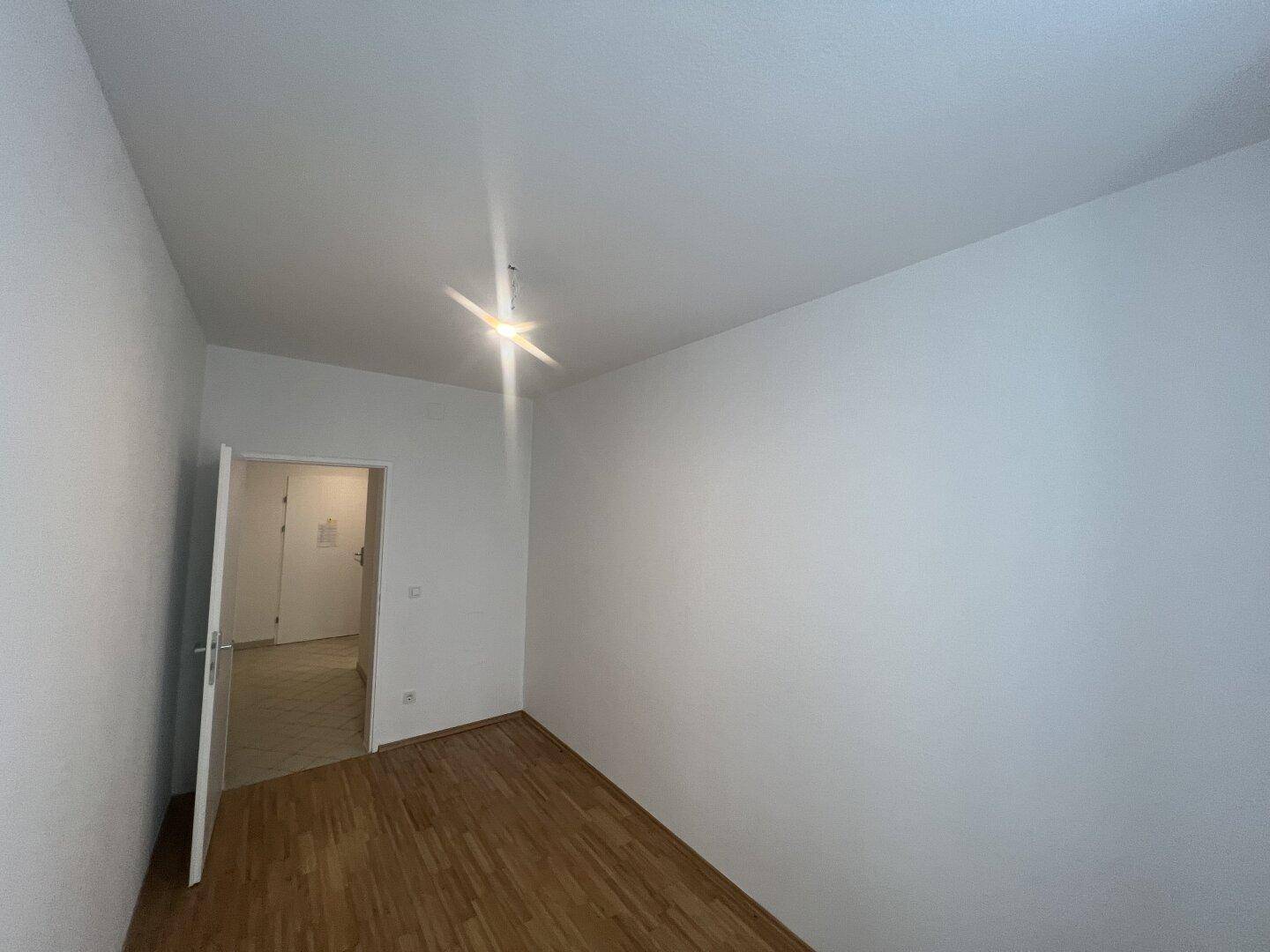 Einfaches Zimmer mit Holzboden und weißen Wänden, bereit zur individuellen Gestaltung.