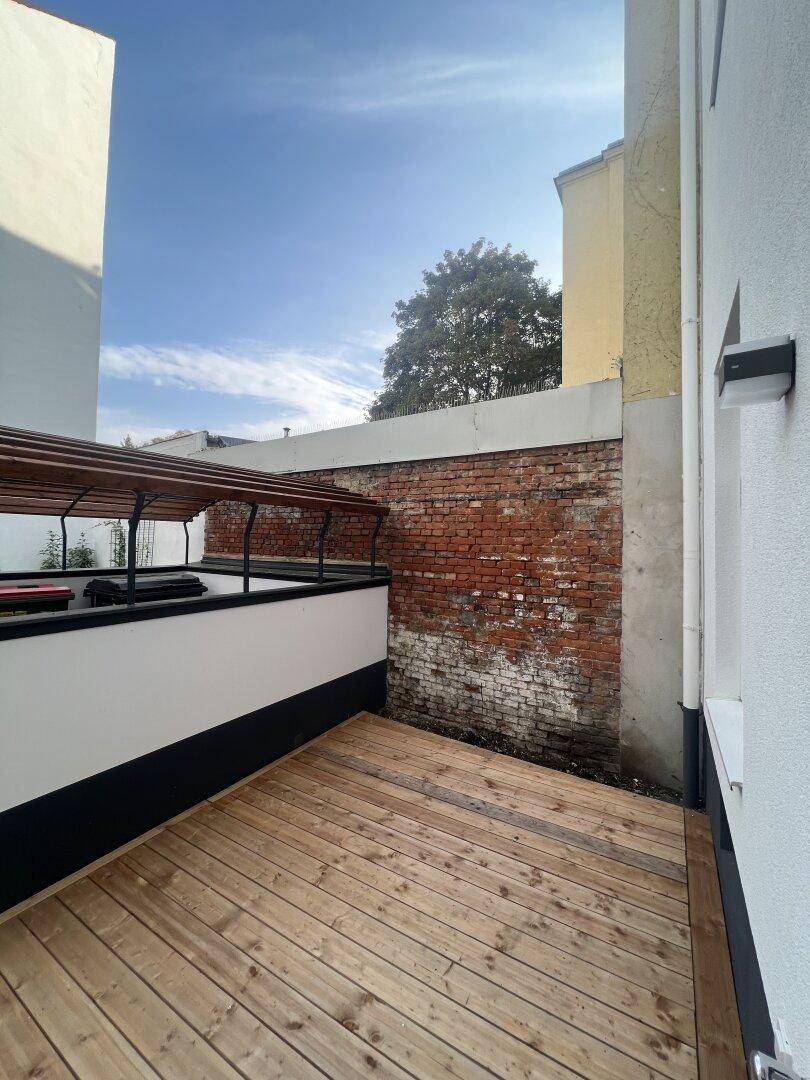 Private Holzterrasse mit Backsteinwand und offenem Himmel, perfekt für Outdoor-Entspannung.