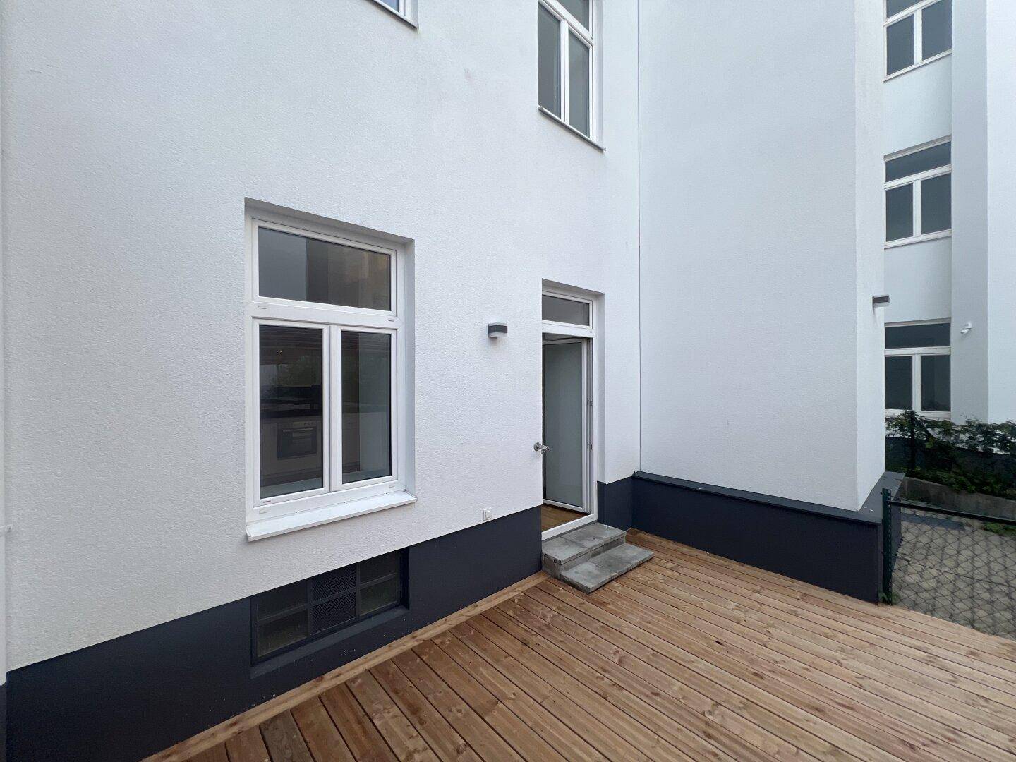 Holzterrasse am Gebäude mit direktem Zugang zur Wohnung und Blick auf den Innenhof.