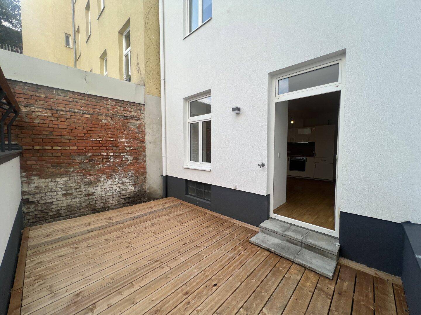 Sonniger Terrassenbereich mit Holzboden und direktem Zugang zur Wohnung, umgeben von Mauern.