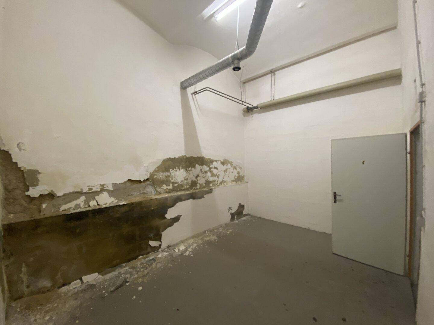 Unfertiger Kellerbereich mit schadhaften Wänden, Betonboden und sichtbaren Installationen.