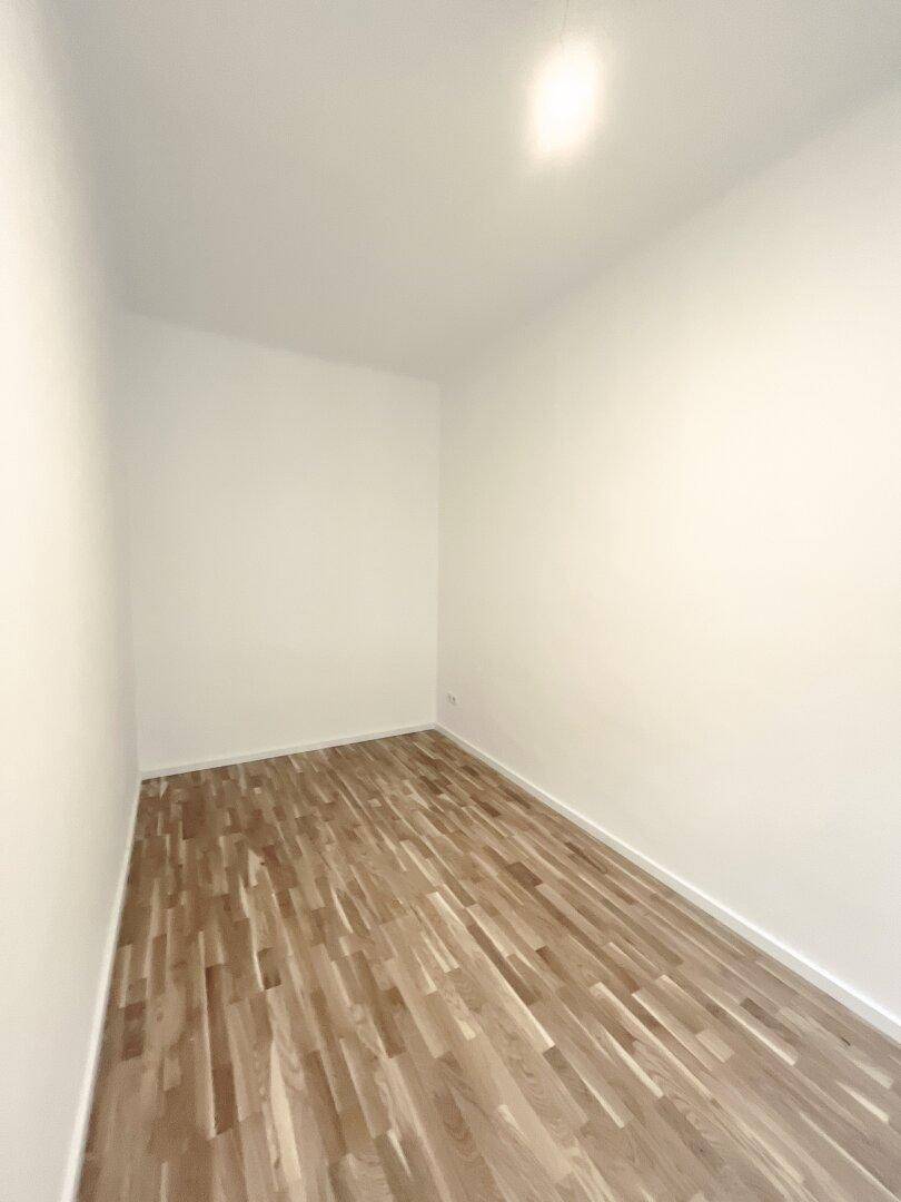 Kleineres, leeres Zimmer mit Parkettboden und weißen Wänden, ideal als Kinder- oder Gästezimmer.