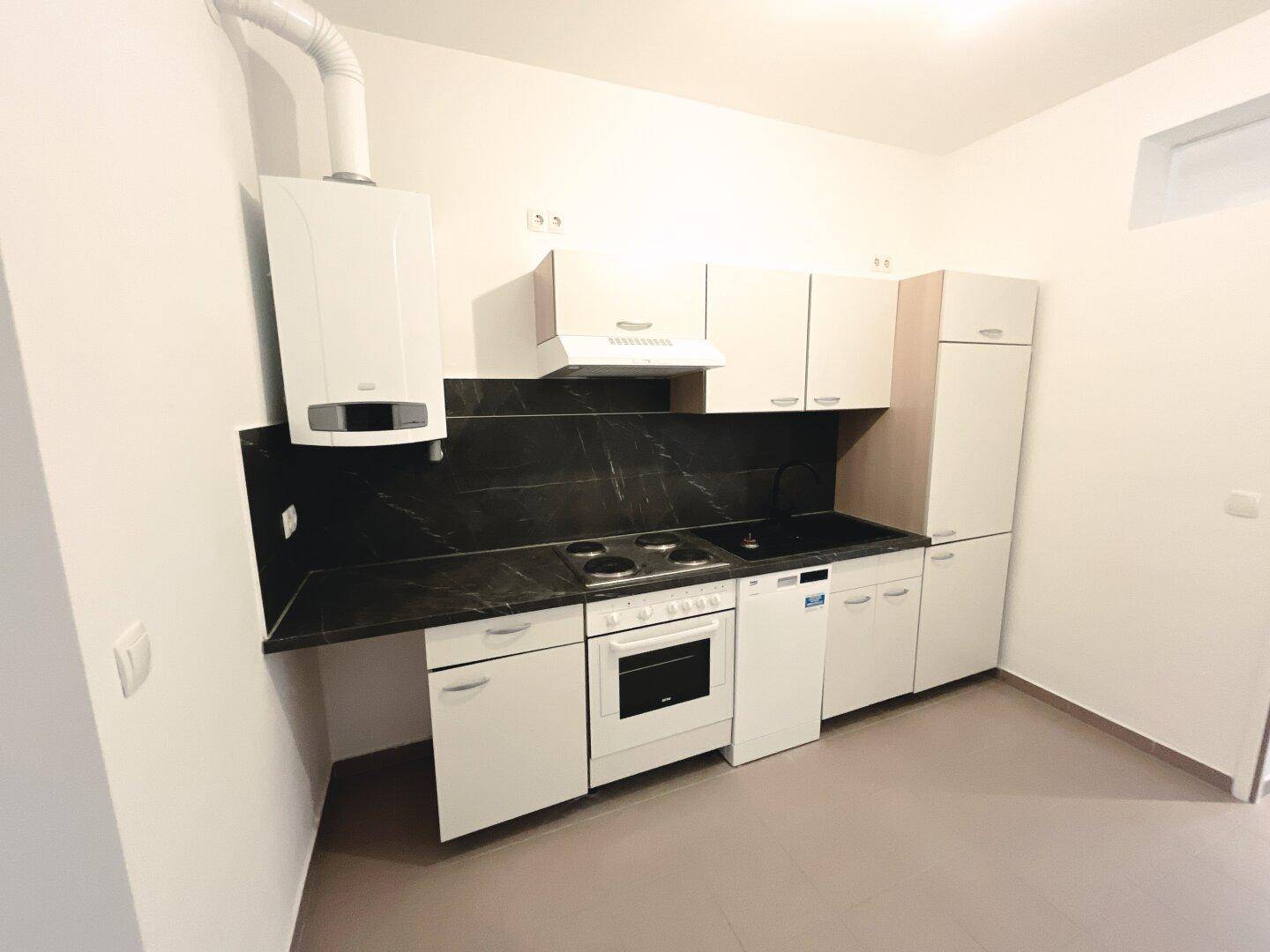 Funktionale Einbauküche mit weißen Schränken, dunkler Arbeitsplatte und integrierten Geräten.