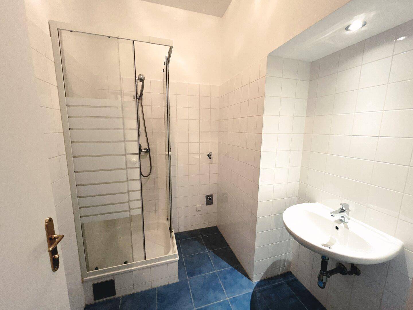 Badezimmer mit weiß gefliesten Wänden, blauen Bodenfliesen und einer Duschkabine.