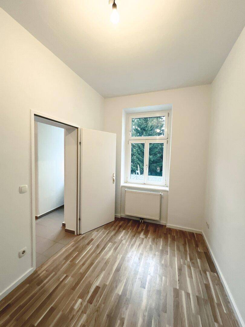 Geräumiges Zimmer mit Parkettboden und Blick ins Grüne, bietet eine ruhige Atmosphäre.