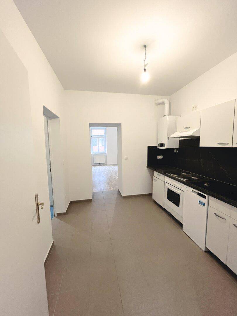 Küche mit Fliesenboden und Blick in ein weiteres Zimmer, ausgestattet mit Einbaumöbeln.