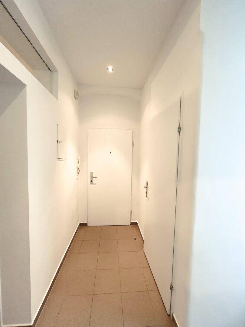 Heller Flur mit Fliesenboden und Eingangstür, führt zu den verschiedenen Räumen der Wohnung.