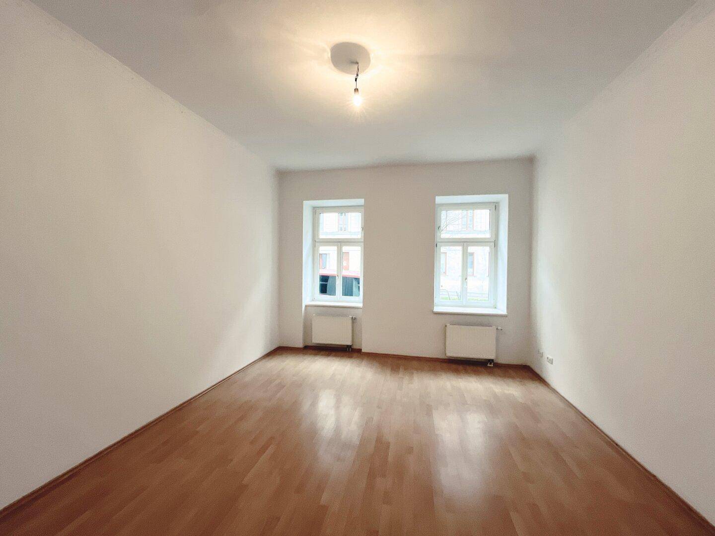 Geräumiges, helles Zimmer mit Parkettboden und zwei Fenstern, bietet viel Tageslicht.