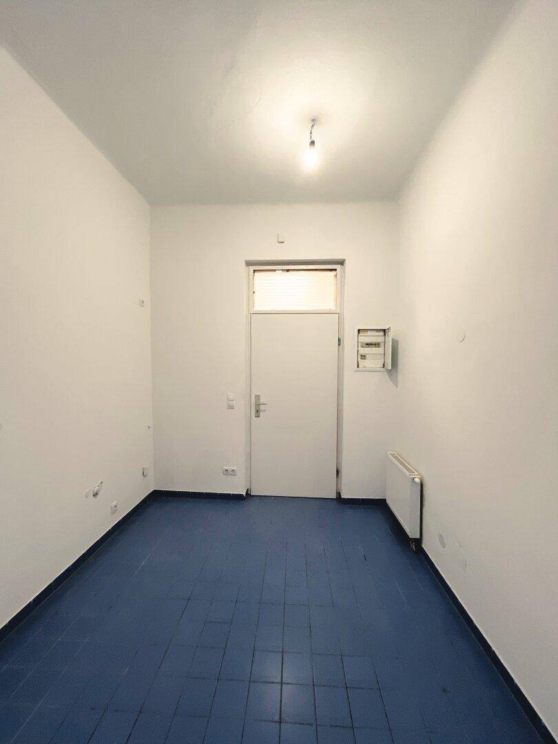 Heller Flur mit blauen Fliesen und einer Eingangstür, ausgestattet mit einem Heizkörper.