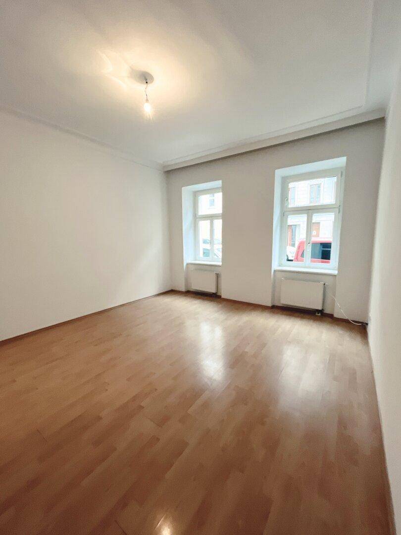 Freundliches, leeres Zimmer mit Parkettboden und zwei Fenstern, bietet eine neutrale Basis.