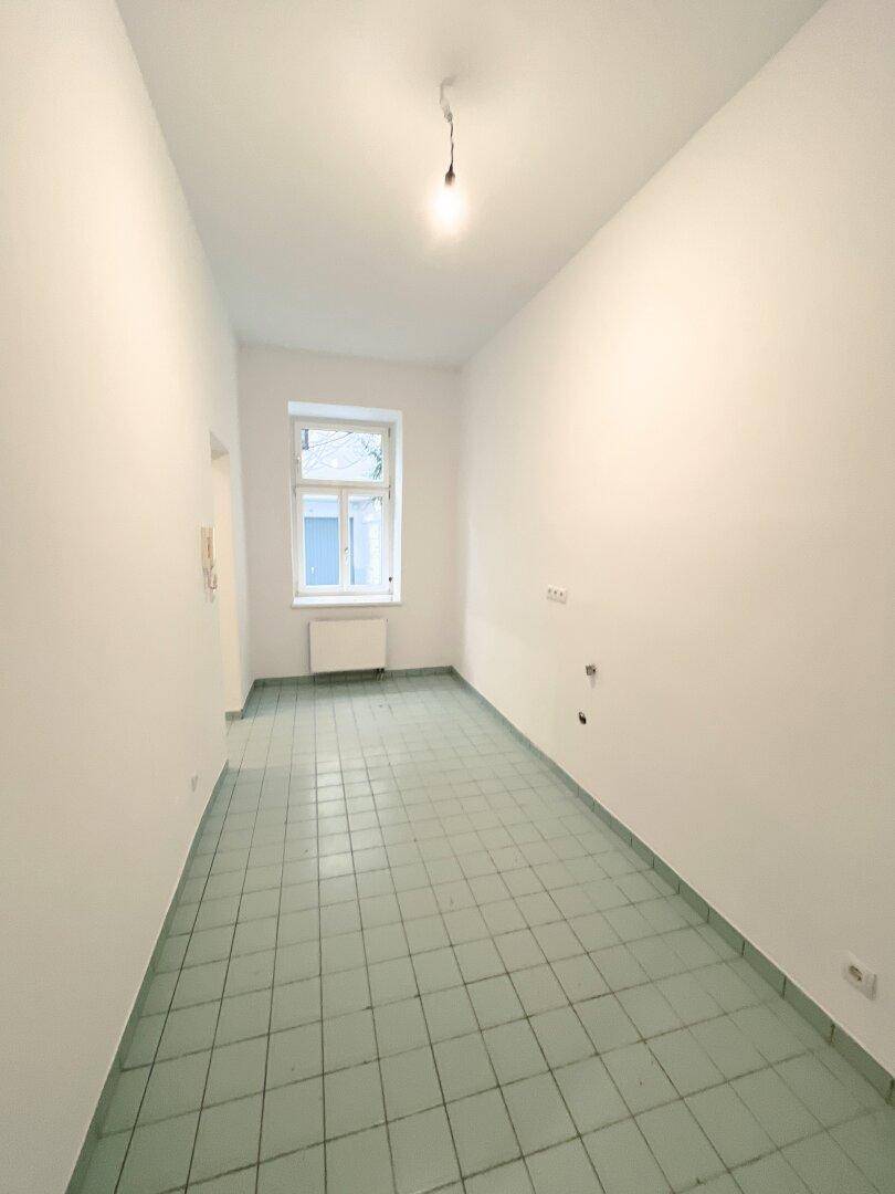 Langer, heller Raum mit grünen Fliesen und einem Fenster, möglicherweise für eine Küche oder Hauswirtschaftsraum.