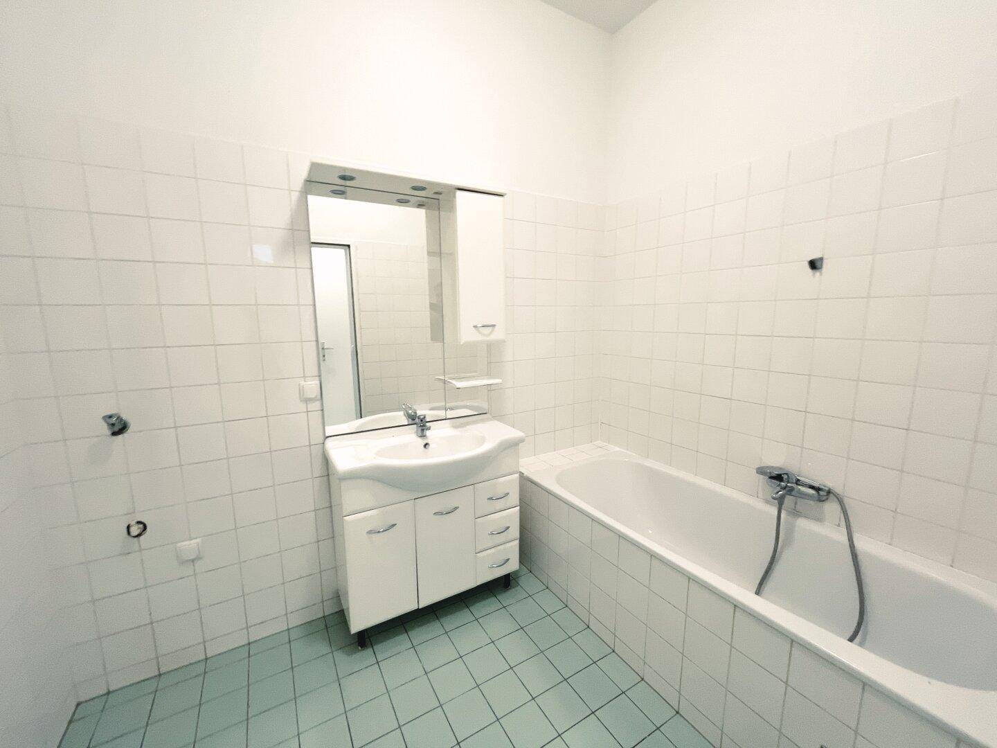 Badezimmer mit Badewanne, Waschbecken und Spiegel, komplett gefliest in Weiß und Hellgrün.