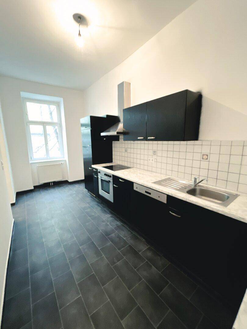Moderne Küche mit schwarzen Schränken, Fliesenboden und integrierten Geräten.