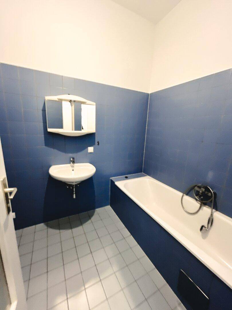 Badezimmer mit blauen Fliesen, Badewanne und Waschbecken, in gutem Zustand.
