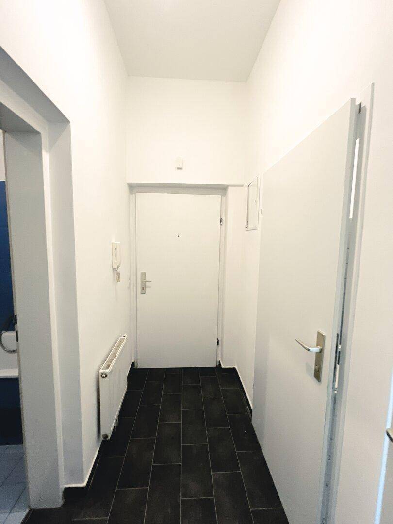 Schmaler Flur mit dunklem Fliesenboden und weißer Tür, verbindet die Räume der Wohnung.