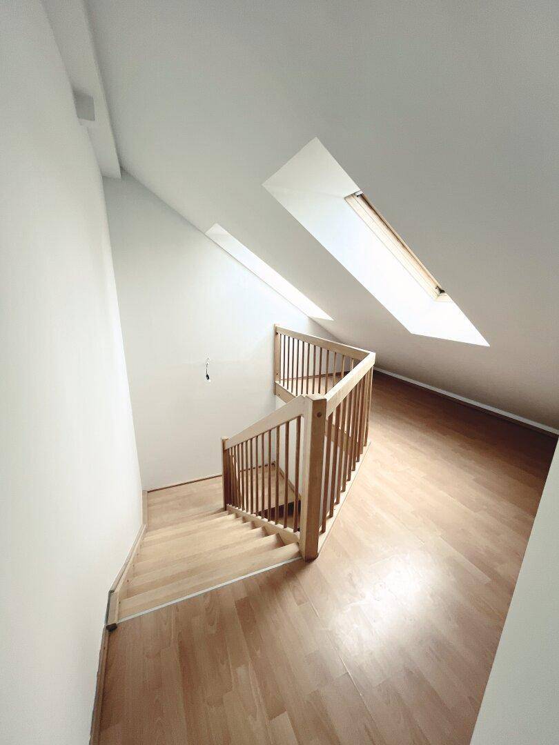 Dachgeschossbereich mit Holztreppe, schrägen Wänden und natürlichem Licht durch Dachfenster.