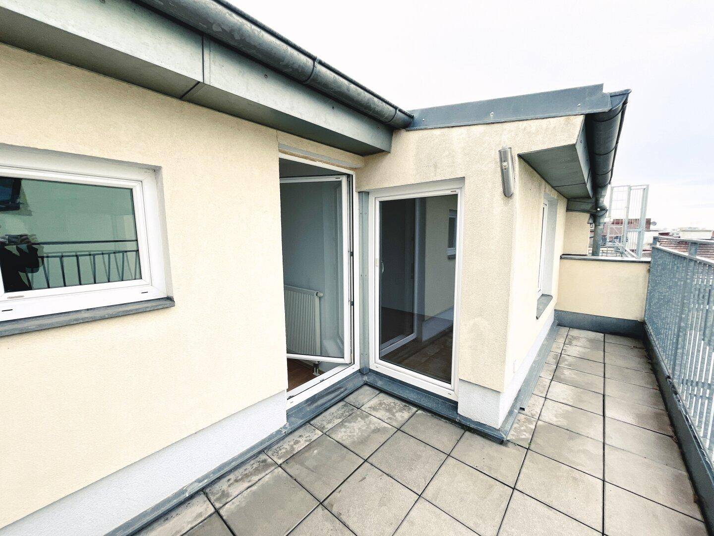 Dachterrasse mit Fliesenboden und Metallgeländer, zugänglich von Innenräumen.