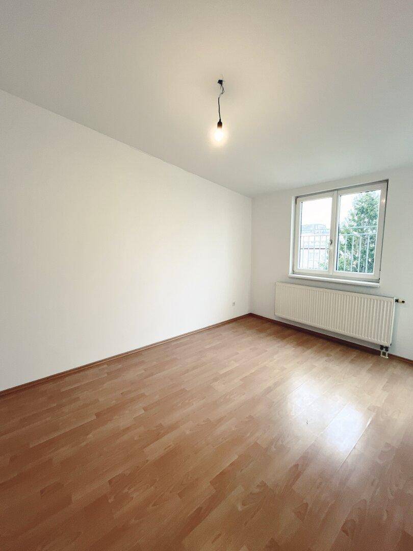 Helles Schlafzimmer mit Laminatboden und einem Fenster mit Blick ins Grüne.