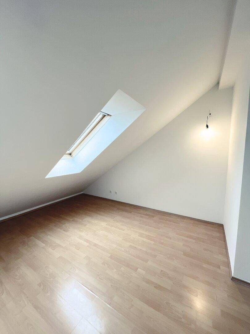 Dachgeschosszimmer mit schräger Decke, Dachfenster und hellem Laminatboden.
