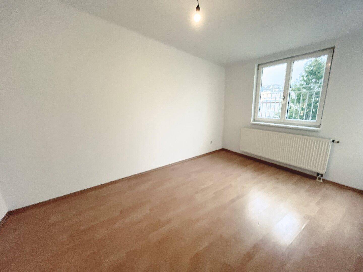 Geräumiges Schlafzimmer mit hellem Laminatboden und einem Fenster, das viel Licht hereinlässt.